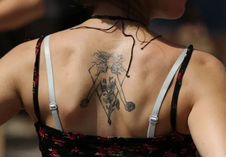 Tatuaż bliźnięta na plecach kobiety, przedstawiający postać z kwiatami i kulą.