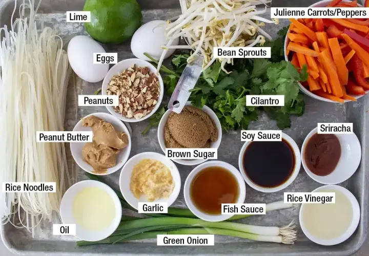 Składniki do pad thai: makaron ryżowy, jajka, orzeszki ziemne, masło orzechowe, olej, czosnek, zielona cebulka, kiełki fasoli, kolendra, cukier brązowy, sos sojowy, sos rybny, ocet ryżowy, sriracha, marchewka i papryka.