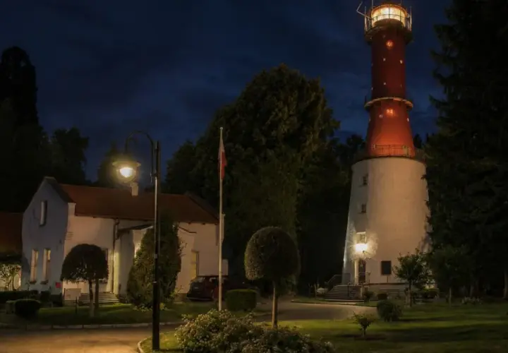 Latarnia morska Jastrzębia Góra nocą, z oświetlonym budynkiem i charakterystyczną czerwoną wieżą.