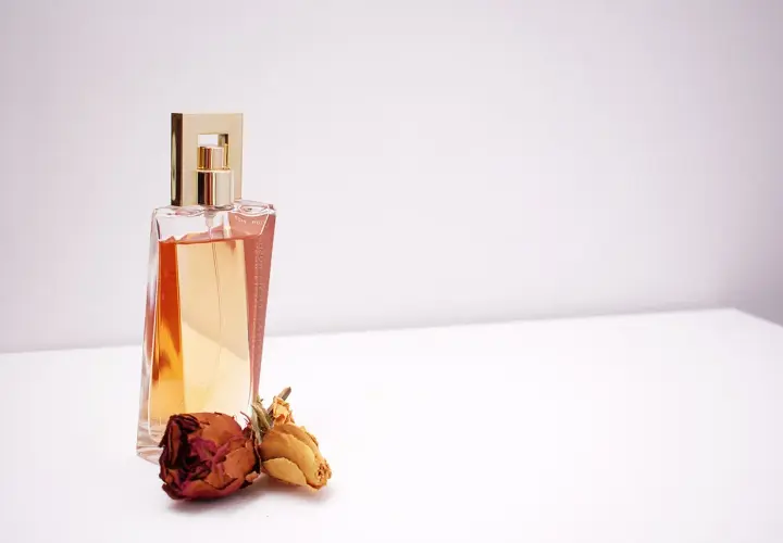 Elegancka butelka perfum z płynem w kolorze bursztynu, ozdobiona złotą nakrętką. Obok leżą dwie zasuszone róże, sugerujące nuty piżma w zapachu.
