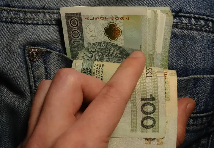 Dłoń wyciąga banknoty 100 zł z kieszeni dżinsów. Może to symbolizować walkę z zatorami płatniczymi lub po prostu gotówkę.