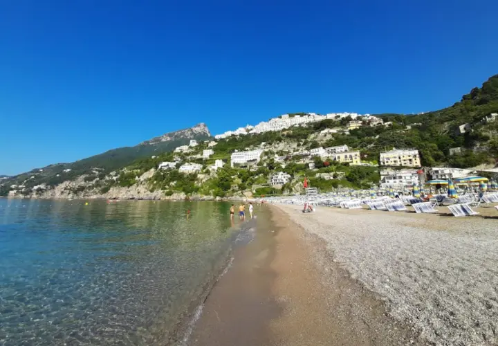 Plage de galets à Vietri sul Mare, Italie, avec des maisons blanches perchées sur la colline verdoyante et la mer bleue étincelante.