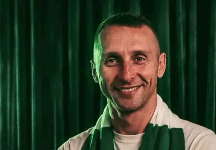 Uśmiechnięty mężczyzna w szaliku Lechii Gdańsk na tle zielonej kurtyny.