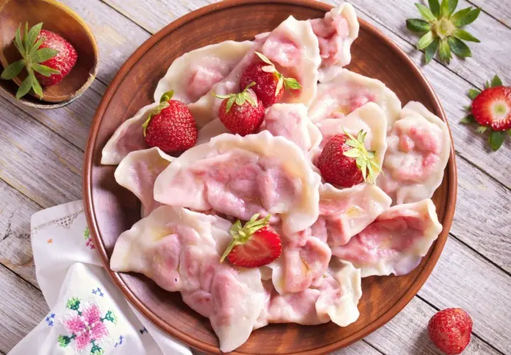 Pyszne pierogi z truskawkami, ozdobione świeżymi owocami, wyglądają apetycznie na glinianym talerzu.