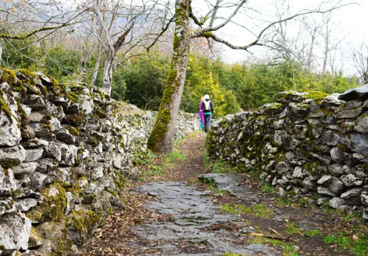 Sendero de piedra cubierto de musgo, parte de la ruta Garganta de Escuain. Dos excursionistas avanzan por el camino.