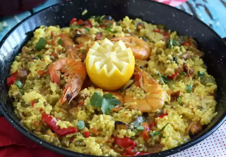 Arroz con pollo y marisco en paellera, adornado con limón y perejil. Un festín de sabores.