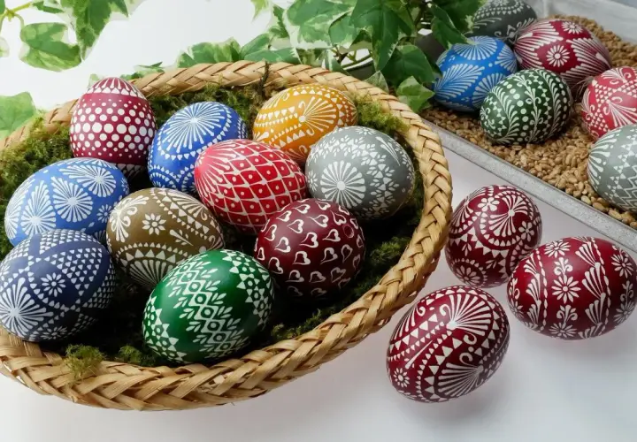 Kosz pełen barwnych pisanki kraszanki z tradycyjnymi wzorami. Wśród nich jajka zdobione białymi ornamentami: kwiatami, serduszkami i geometrycznymi motywami.
