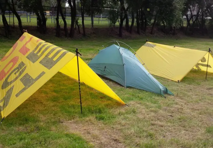 Trzy namioty na trawie. Dwa żółte z napisem "OUTDOOR" i jeden zielony. Namiot z tarpa gotowy na przygodę.