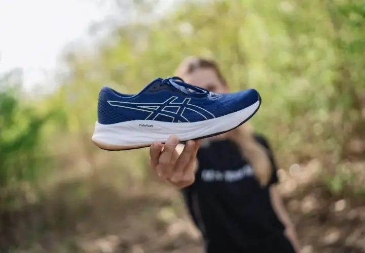 Dłoń trzymająca niebieski but Asics z białym logo. Idealna rozmiarówka Asics dla biegaczy.