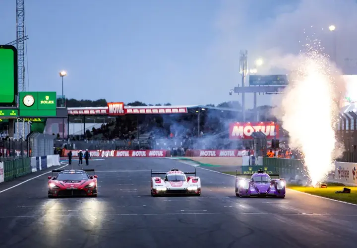 Tres coches de carreras compiten en Le Mans, con fuegos artificiales iluminando la pista. El horario de Le Mans se acerca.