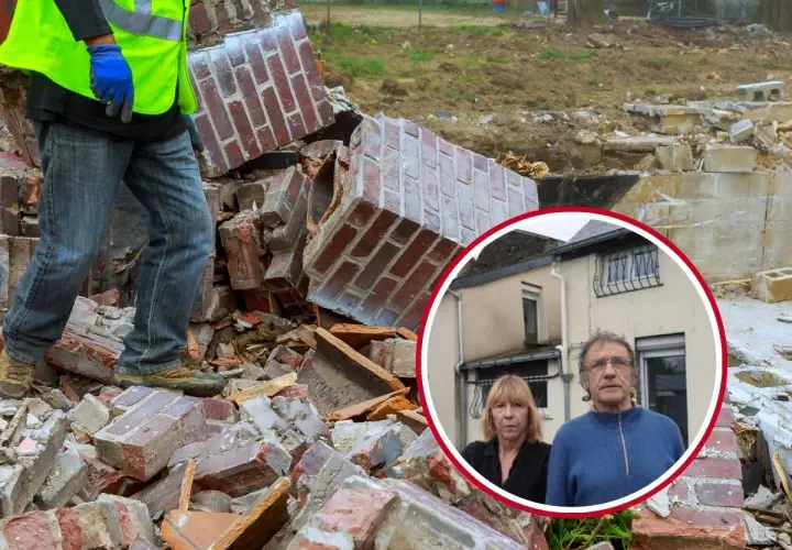 Pareja preocupada frente a los escombros de su hogar tras un cru catastro. Un trabajador con chaleco fluorescente camina entre los restos.