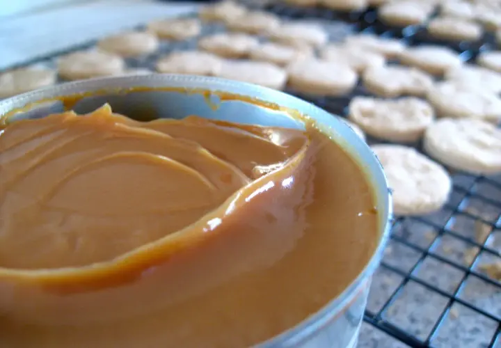Un pot de confiture de lait onctueuse, prêt à garnir des biscuits secs disposés sur une grille.