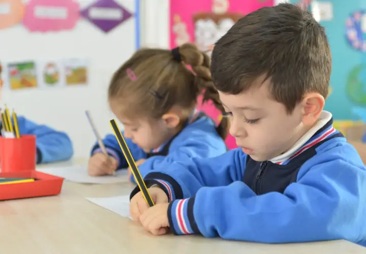 Niños concentrados en sus cuadernos, un momento de aprendizaje y adaptación en el aula.