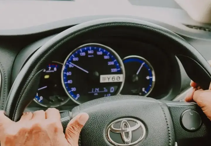 Ręce na kierownicy Toyoty, widoczne zegary i wskaźniki. Elektryczne wspomaganie kierownicy ułatwia jazdę.