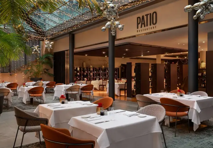 Atmosfera elegante al Patio Restaurant, un'ottima opzione per chi cerca dove mangiare a Bolzano. Tavoli apparecchiati sotto luci soffuse e piante rigogliose.