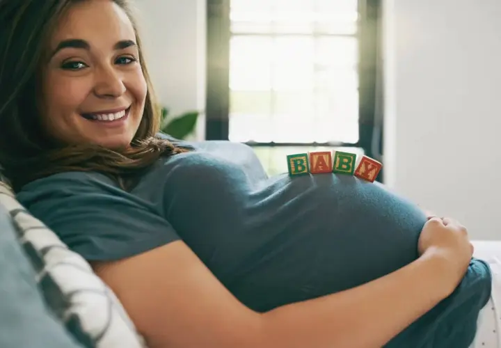 Uśmiechnięta surogatka z klockami "BABY" na brzuchu.