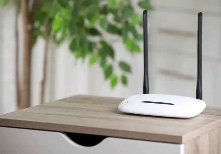 Biały router z dwiema antenami na drewnianym blacie. Dowiedz się, jak działa router bez karty SIM, tworząc domową sieć Wi-Fi.