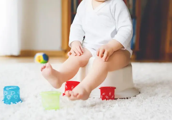 Liten bebis på pottan, redo att sluta med napp. Färgglada leksaker och en mjuk matta skapar en trygg miljö för potträning.