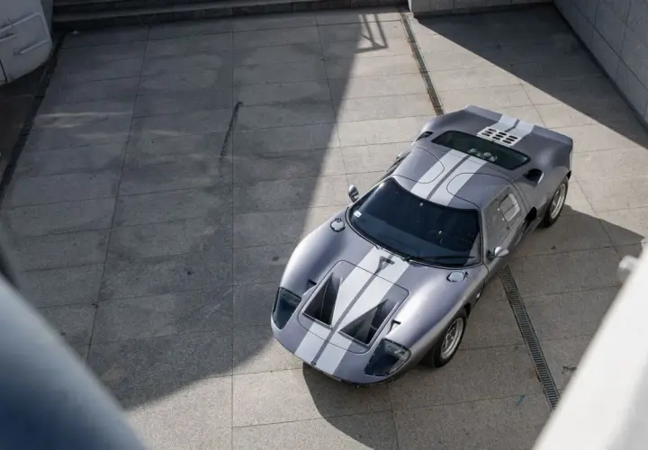 Srebrny Ford GT40 z białymi pasami, gotowy do wyścigu. Ikona motoryzacji na betonowym placu.