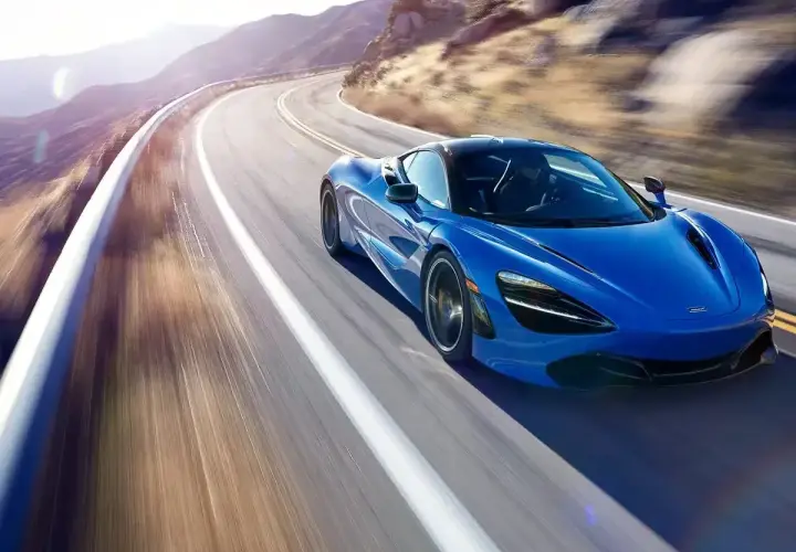 Niebieski McLaren 720S pędzi po krętej górskiej drodze, tworząc rozmyte smugi światła i cienia.
