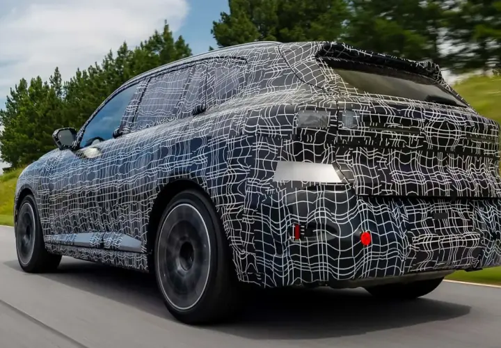 La nuova BMW X5 2026, con la sua mimetica di test, sfreccia su una strada panoramica, anticipando il futuro del design.
