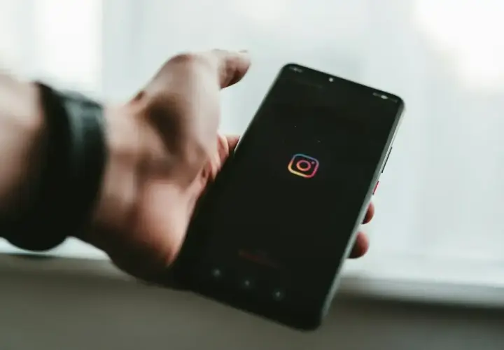 Dłoń trzyma smartfon z logo Instagram. Chcesz wiedzieć, jak zobaczyć relacje na IG?
