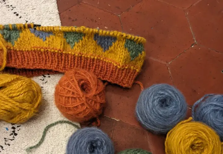 Un tricot jacquard aux motifs géométriques colorés, entouré de pelotes de laine.