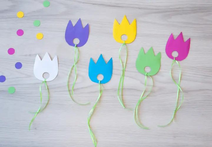 Bunte Papier-Tulpen mit grünen Bändern, perfekt für das Basteln mit Kindern. Bunte Tupfen liegen verstreut.