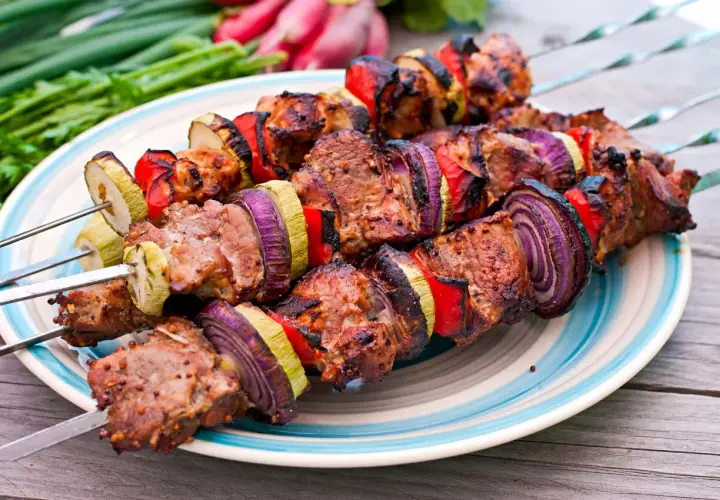 Brochettes d'agneau grillées avec oignons rouges, poivrons et courgettes sur une assiette bleue et blanche.