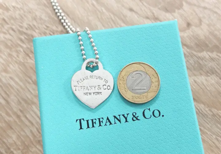 Srebrne serce z napisem "Please Return to Tiffany & Co. New York" na turkusowym pudełku Tiffany & Co. z monetą 2 złote.