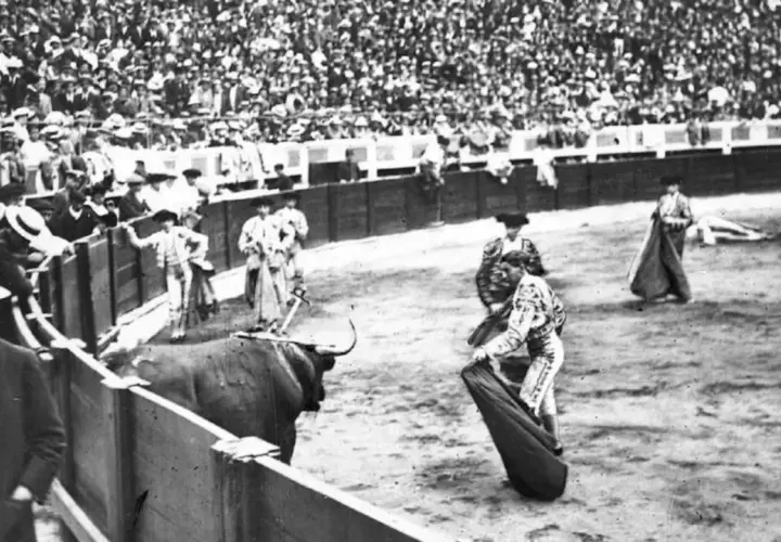 En la plaza, un toro bravo se prepara para la cornada. Joselito el gallo, con su traje de luces, se enfrenta al animal ante una multitud expectante.