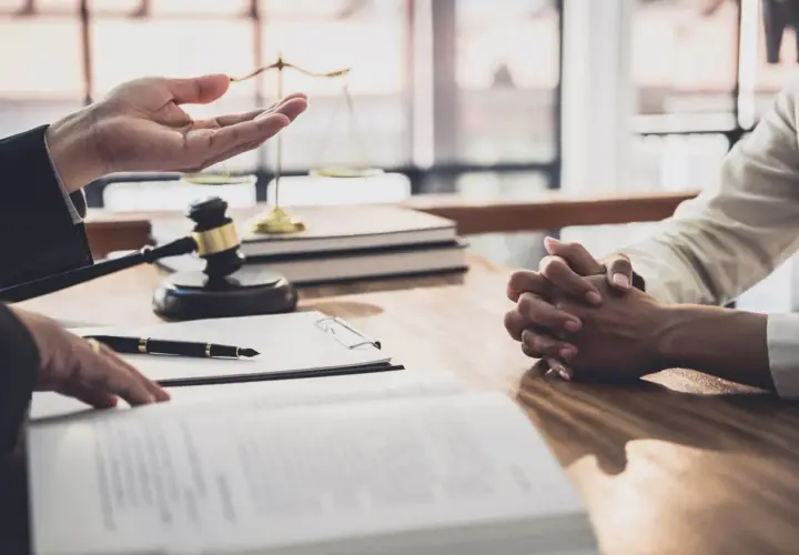 Prawnik omawia z klientem formalności związane z wnioskiem o stwierdzenie nabycia spadku. Na stole leżą dokumenty, młotek sędziowski i waga sprawiedliwości.