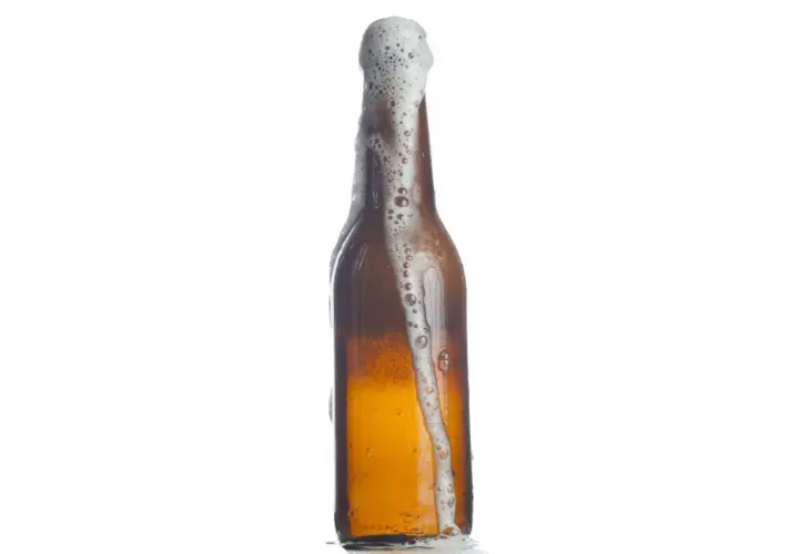 Bière débordant d'une bouteille, la mousse blanche montant. Le pourcentage d'eau dans la bière est élevé, comme le montre cette effervescence.