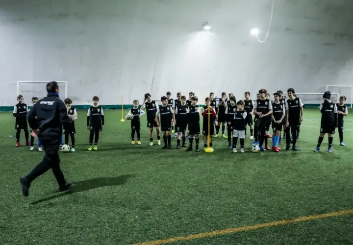 Trener prowadzi trening piłkarski metodą Coerver Coaching, instruując młodych zawodników na boisku.