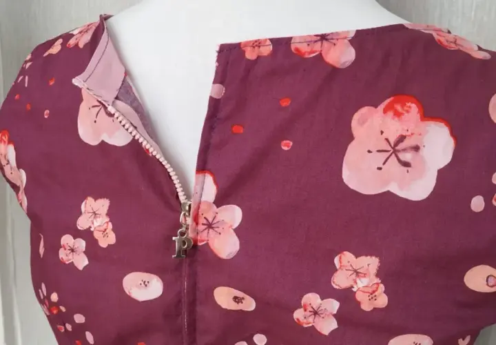 A plum-colored dress with a floral print features a centered zipper with a silver "P" charm.