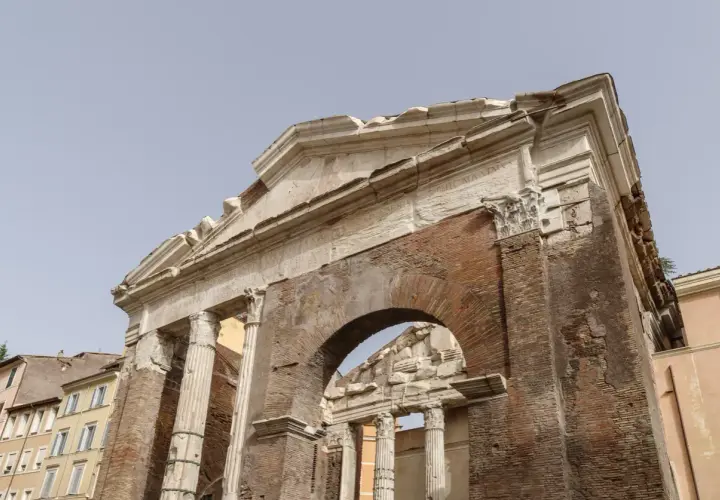 Antica struttura in mattoni e marmo, con colonne e un arco, parte del **Portico di Ottavia**.
