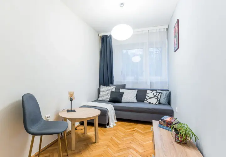 Przytulny pokój z szarą kanapą, stolikiem i krzesłem. Idealne miejsce na relaks, tworzące pozytywny Mokotów.