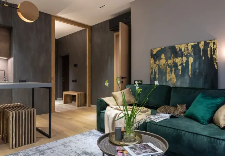 Elegancki salon z butelkowozieloną kanapą, na której leży kot. Złoto-granatowy obraz i jasne dodatki pokazują, jaki kolor pasuje do zielonego butelkowego.