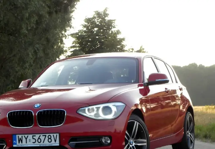Czerwone BMW 118d na tle drzew i pól.