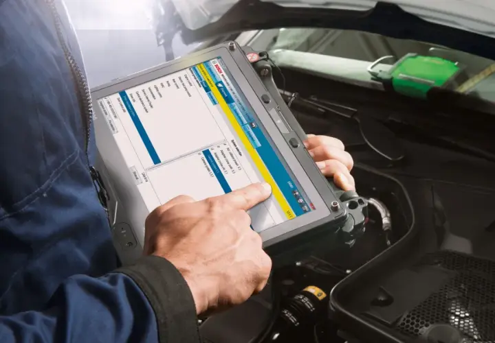 Mechanik sprawdza wtryski za pomocą tabletu diagnostycznego Bosch. Na ekranie widoczne są opcje wyboru systemu, w tym silnik i systemy sterowania.