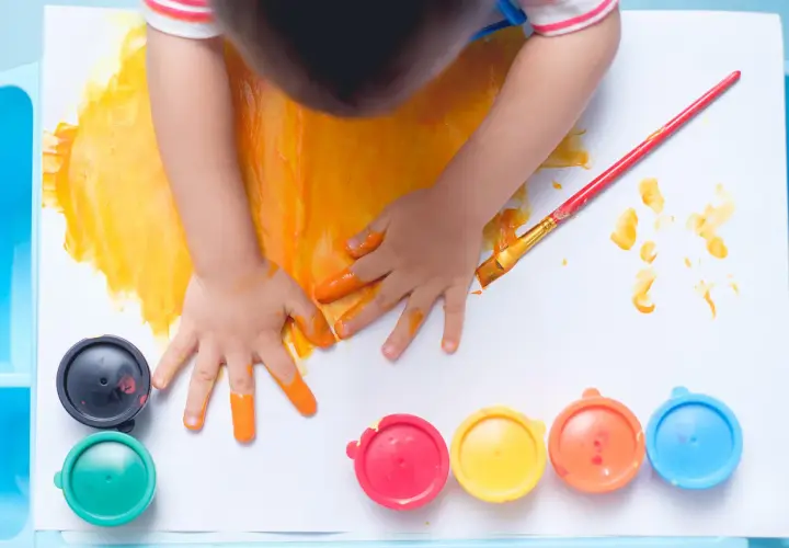 Manos pequeñas pintando con dedos y pincel. Un niño se divierte pintando con niños, rodeado de botes de pintura de colores.