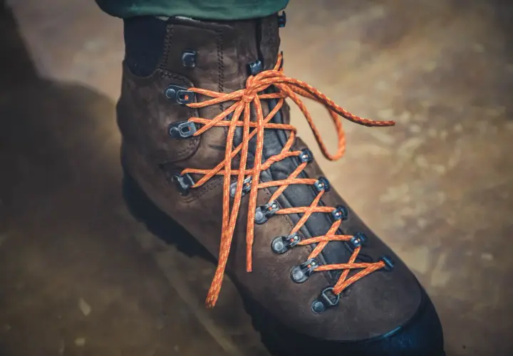 Brązowy but trekkingowy z pomarańczowymi sznurówkami, pokazujący, jak wiązać buty trekkingowe.