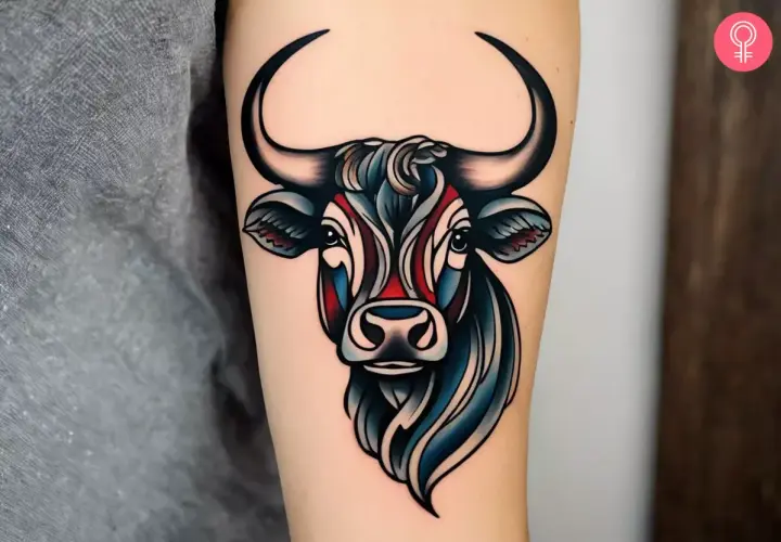 Kolorowy byk tattoo na ramieniu, z czarnymi rogami i niebiesko-czerwonymi akcentami na pysku.