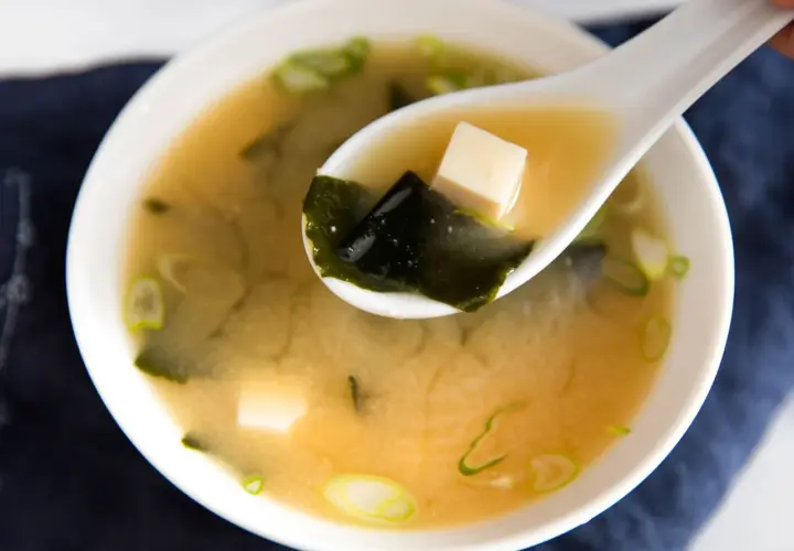 A spoonful of savory miso sauce soup, with tofu cubes and seaweed, ready to be enjoyed.