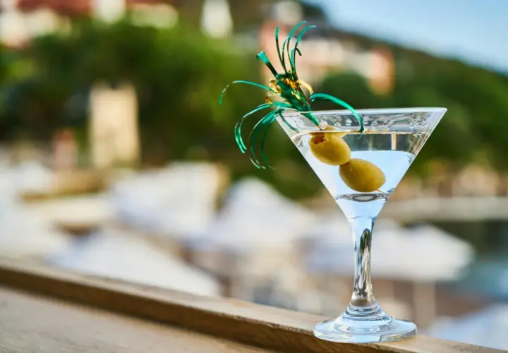 Idealny martini aperitivo z dwiema oliwkami, ozdobiony zielonymi wstążkami, na tle letniego krajobrazu.