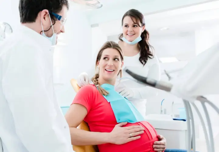 Uśmiechnięta ciężarna pacjentka u dentysty. Dba o zdrowie jamy ustnej, by uniknąć zapalenia dziąseł w ciąży.