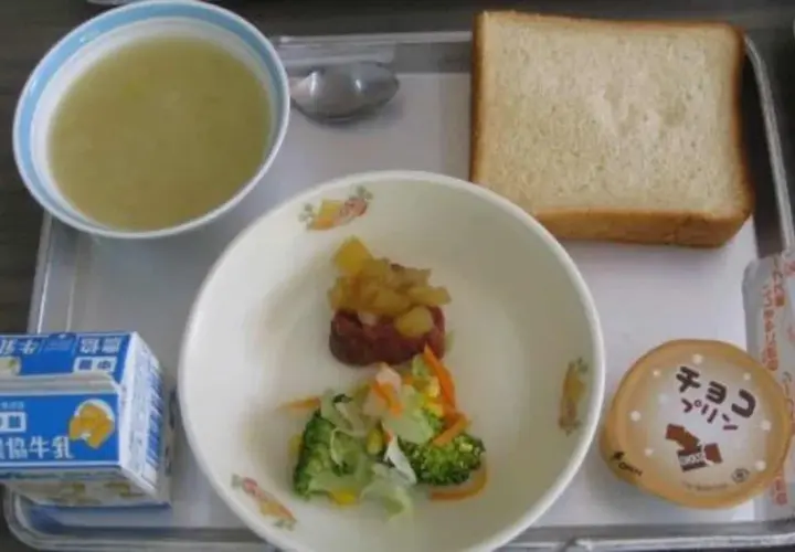 A typical Japanese school lunch tray with soup, bread, vegetables, meat, pudding, and milk.