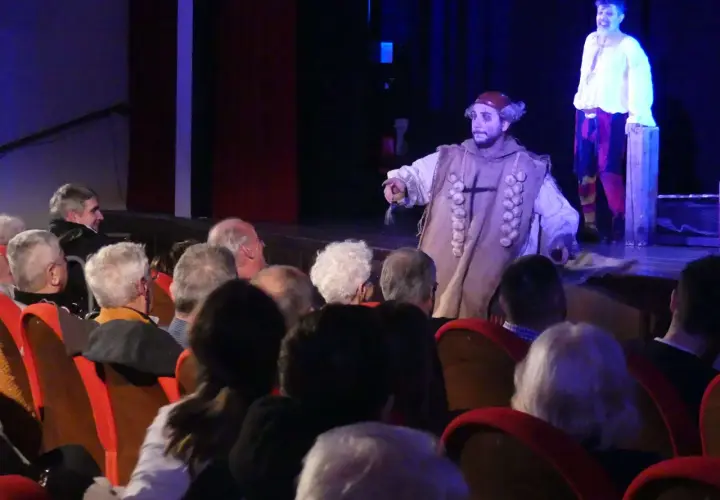 Attori in costume sul palco, il pubblico osserva la rappresentazione teatrale, infrangendo la **quarta parete teatro**.