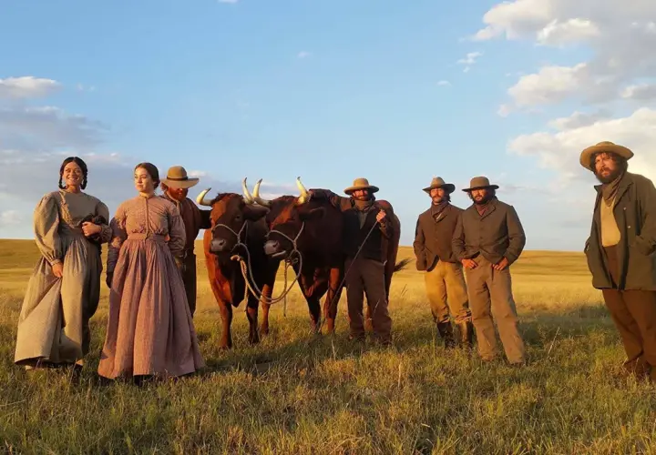 Un gruppo di persone in abiti d'epoca, con due buoi, in un campo dorato. Scena da "La ballata di Buster Scruggs", un film che merita una recensione.