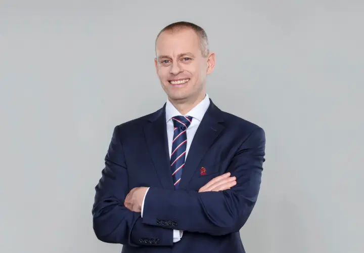Marcin Włodarski, trener, w granatowym garniturze i krawacie, z rękami skrzyżowanymi na piersi, uśmiecha się do obiektywu.